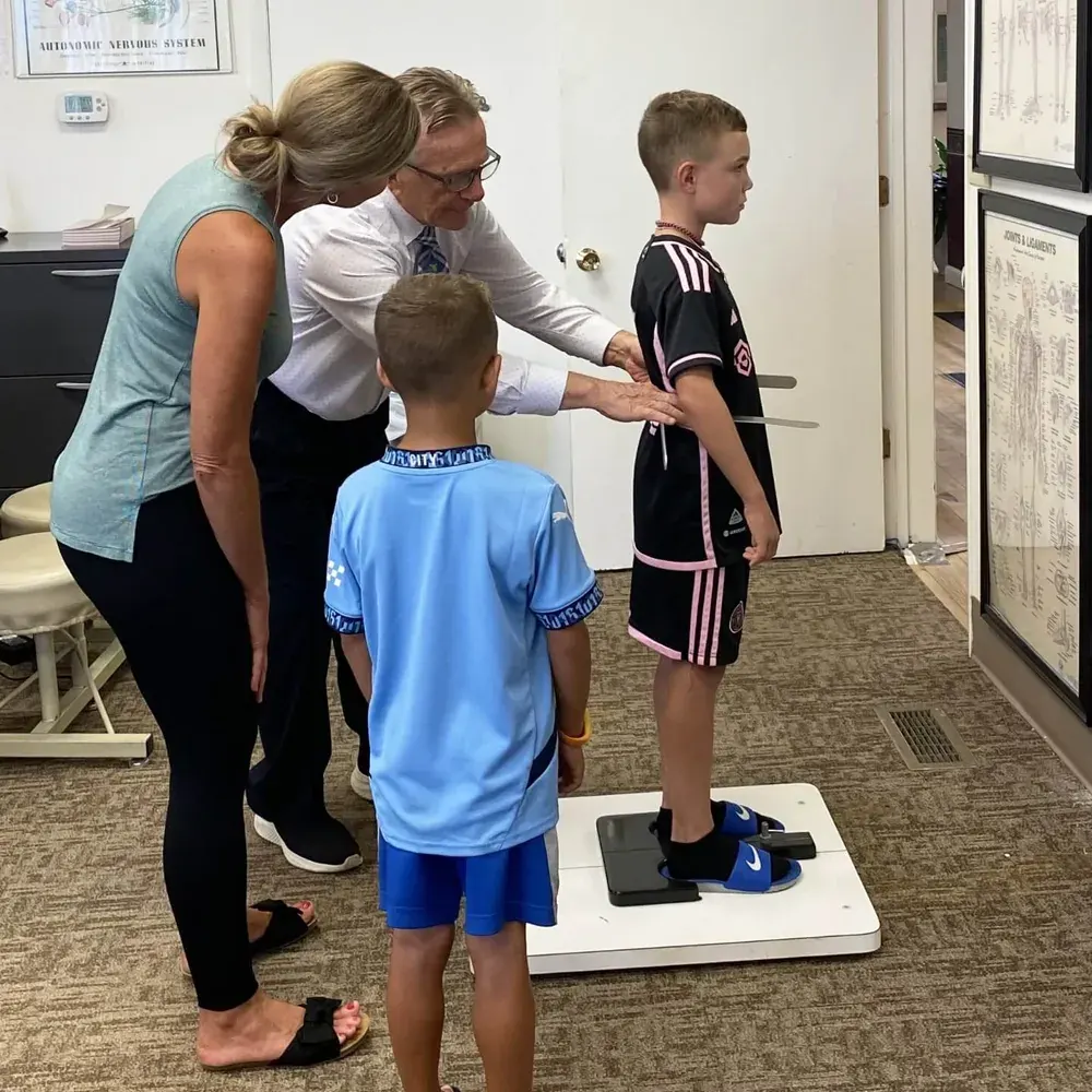 Dr. Toth checking a young patient's posture while his mother watches